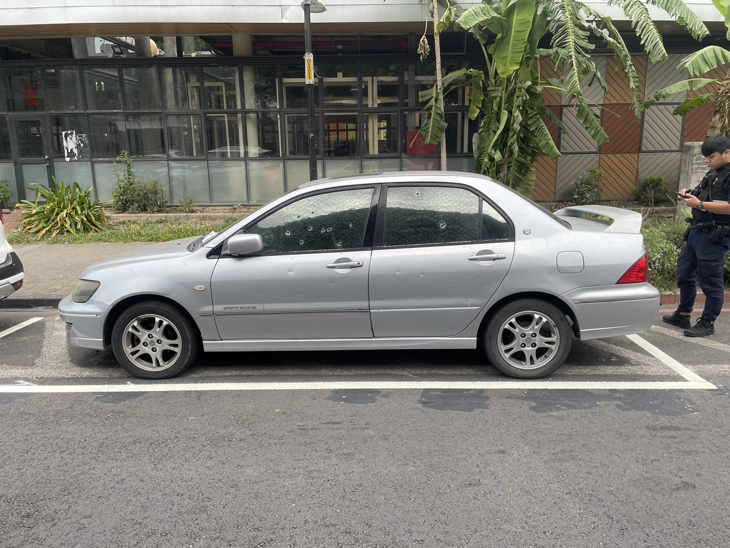 1輛停放在學校附近的銀色轎車，車身和玻璃佈滿了多處彈孔。