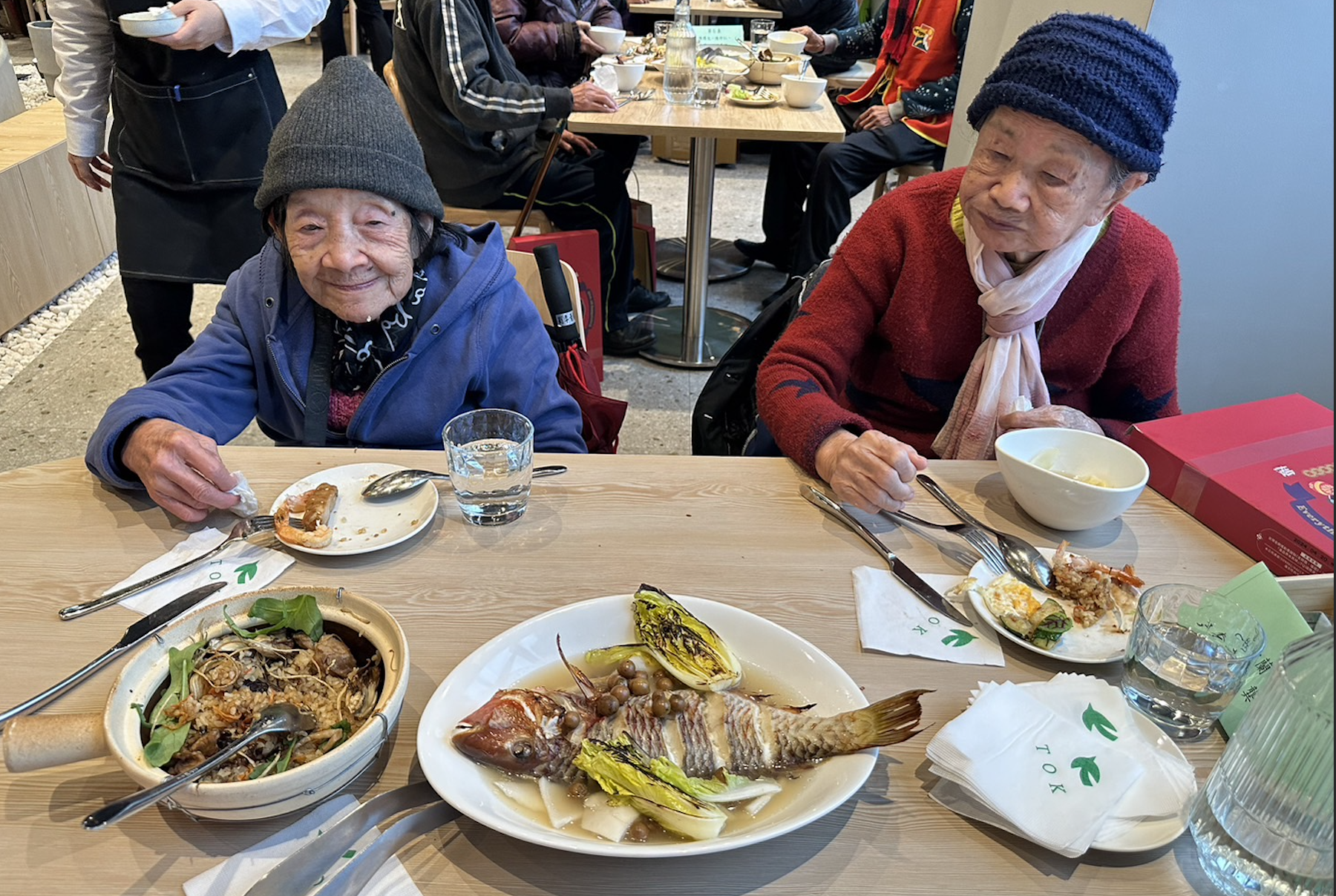 ▲劉李奶奶（左）及龔奶奶（右）品嘗椰湯佐樹子烤魚。(圖/新北市社會局提供)